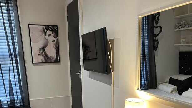 A bedroom with a bed, a bedside table with a lamp, a mirror, and a framed picture on the wall. - Inviting 1-bed Unit in Watford (Watford)