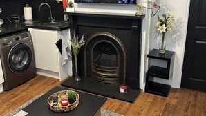 A modern living room with a fireplace, a television mounted above it, a washing machine, and a coffee table with remote controls. - Inviting 1-bed Unit in Watford (Watford)