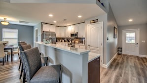 A modern kitchen with white cabinets, a central island, and a dining area with chairs and a table. - Villa Greene, Private Home, Elec. Heated Pool, WIFI, ..... (Cape Coral)