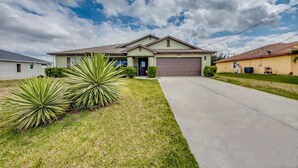 A single-story house with a front garage, a driveway, and a well-maintained lawn with agave plants. - Villa Greene, Private Home, Elec. Heated Pool, WIFI, ..... (Cape Coral)