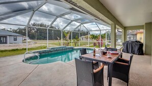 A covered outdoor pool area with a table and chairs, a grill, and a view of the surrounding landscape. - Villa Greene, Private Home, Elec. Heated Pool, WIFI, ..... (Cape Coral)