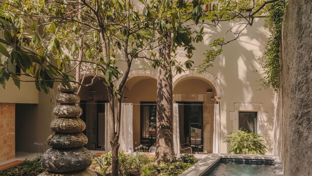 A serene courtyard with a stone water feature, lush greenery, and a pool. - Hotel Palau Fugit (Girona)
