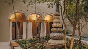 A courtyard with a stone fountain, plants, and a pool. - Hotel Palau Fugit (Girona)