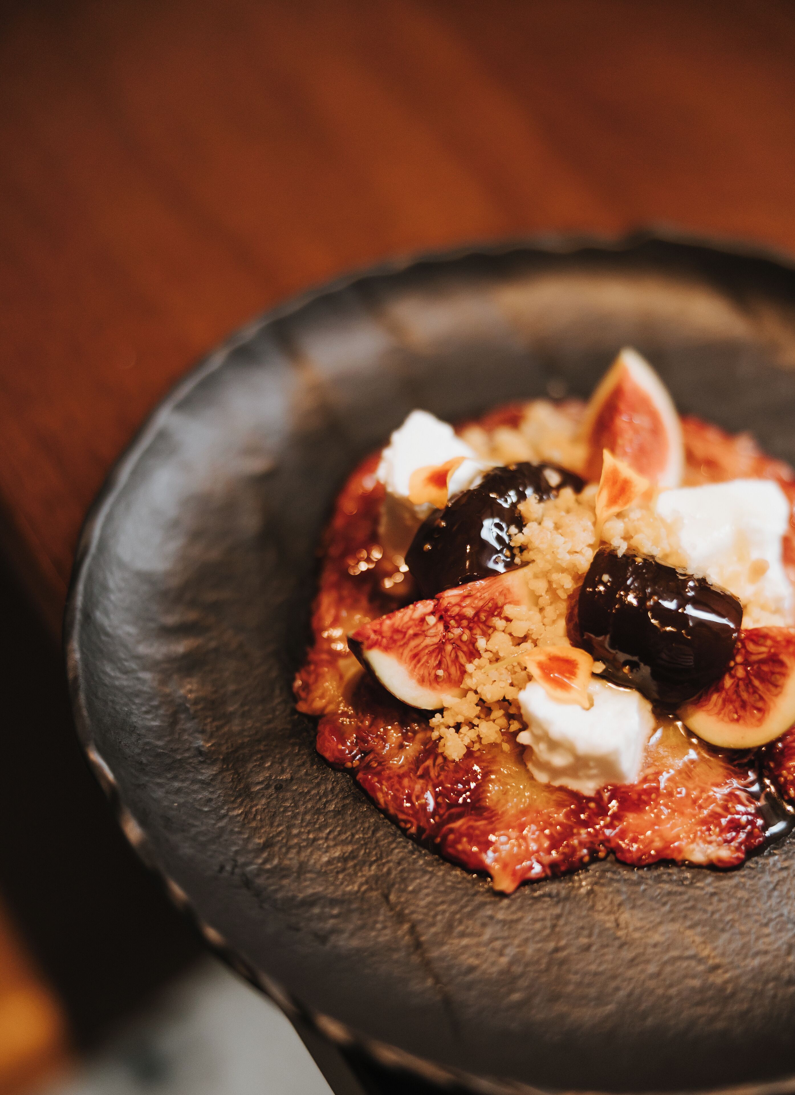 Un postre sobre un plato oscuro, con higos, una cucharada de crema y un hilo de almíbar.