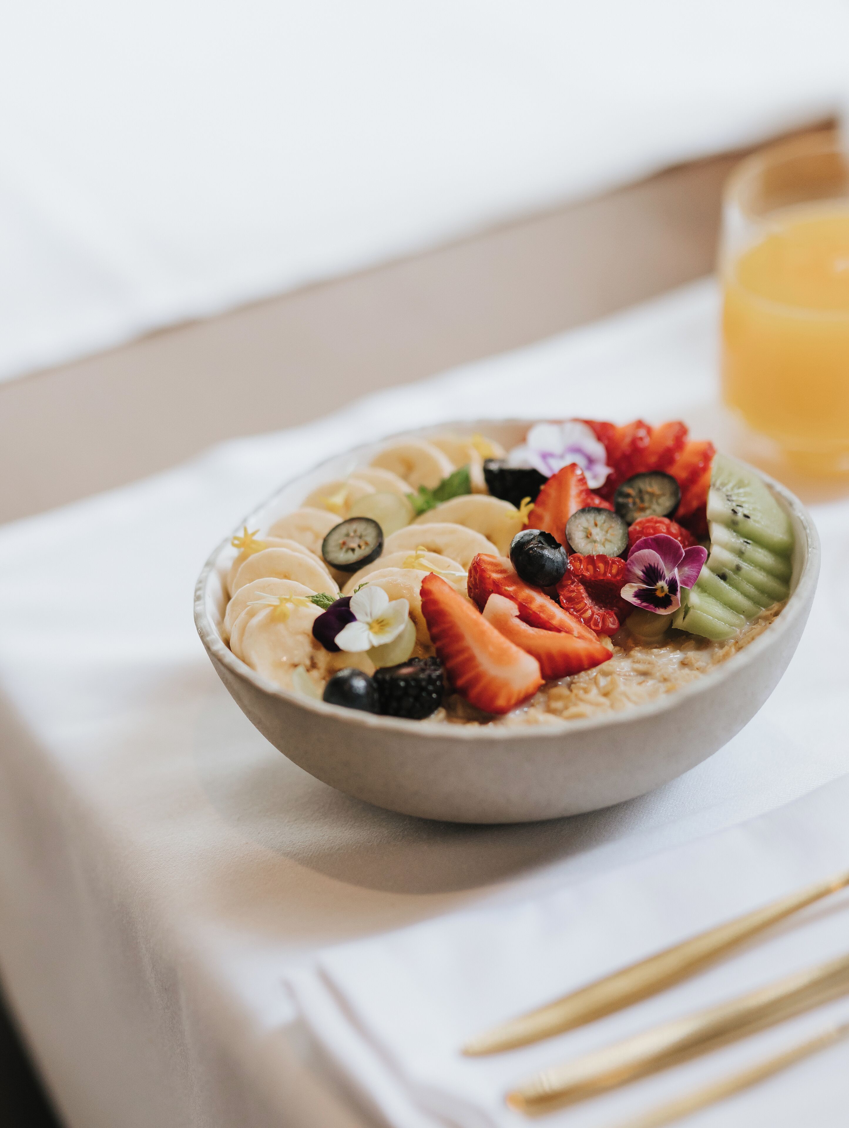 A bowl of oatmeal topped with various fruits and a glass of orange juice on a table.