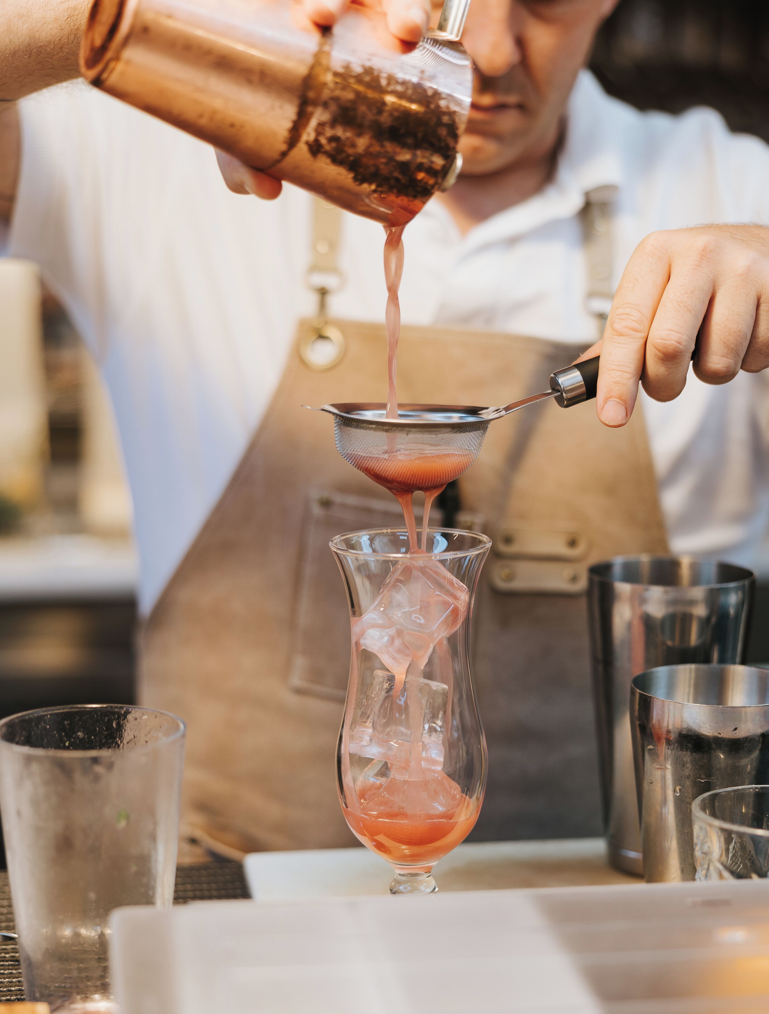 Una persona vertiendo un líquido rosa en un vaso transparente con cubitos de hielo.
