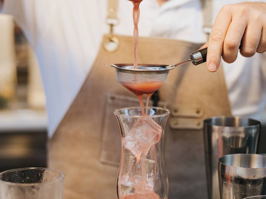 Una persona vertiendo un líquido rosa en un vaso transparente con cubitos de hielo.