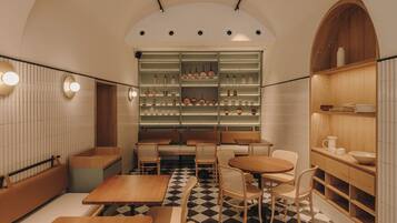 Interior de restaurante con suelo a cuadros, mesas y sillas de madera, y estantes con utensilios de cocina.