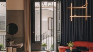 A modern hotel room with a balcony, a sofa, a round table, and a hanging light fixture. - Hotel Palau Fugit (Girona)