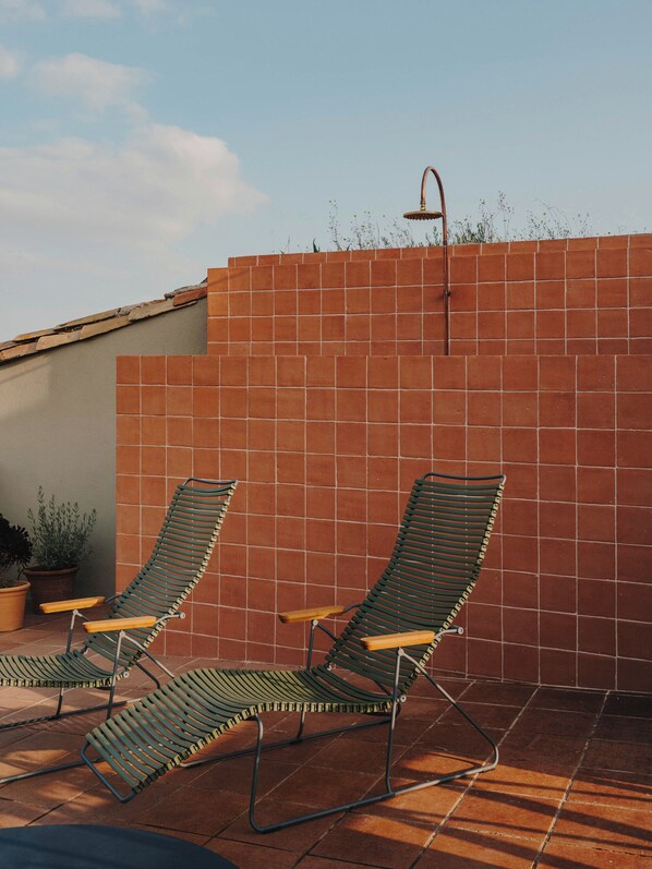 Une terrasse avec deux fauteuils de jardin verts et un mur recouvert de carreaux.