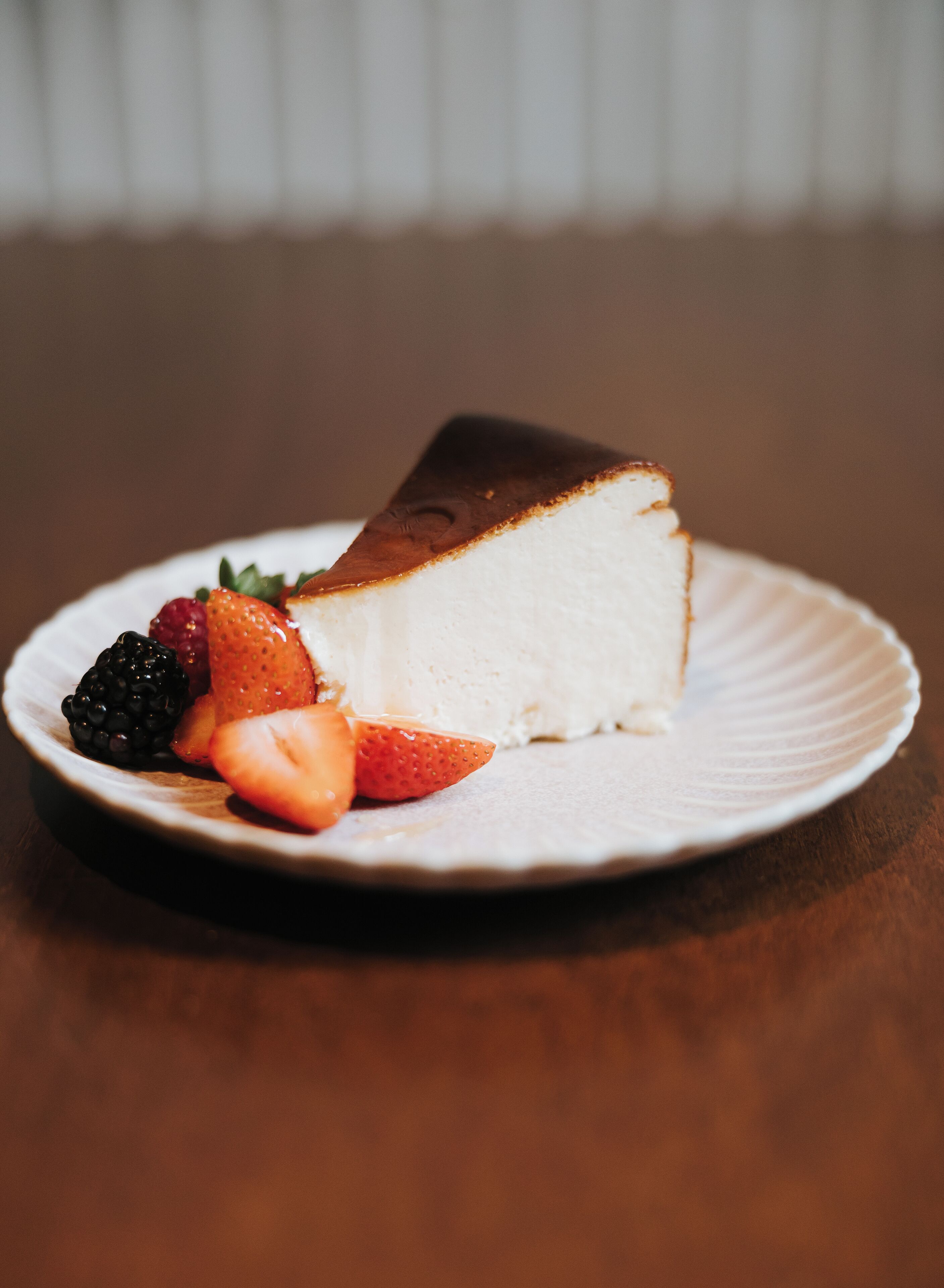 Une part de gâteau au fromage sur une assiette blanche, accompagnée de fraises et de mûres.