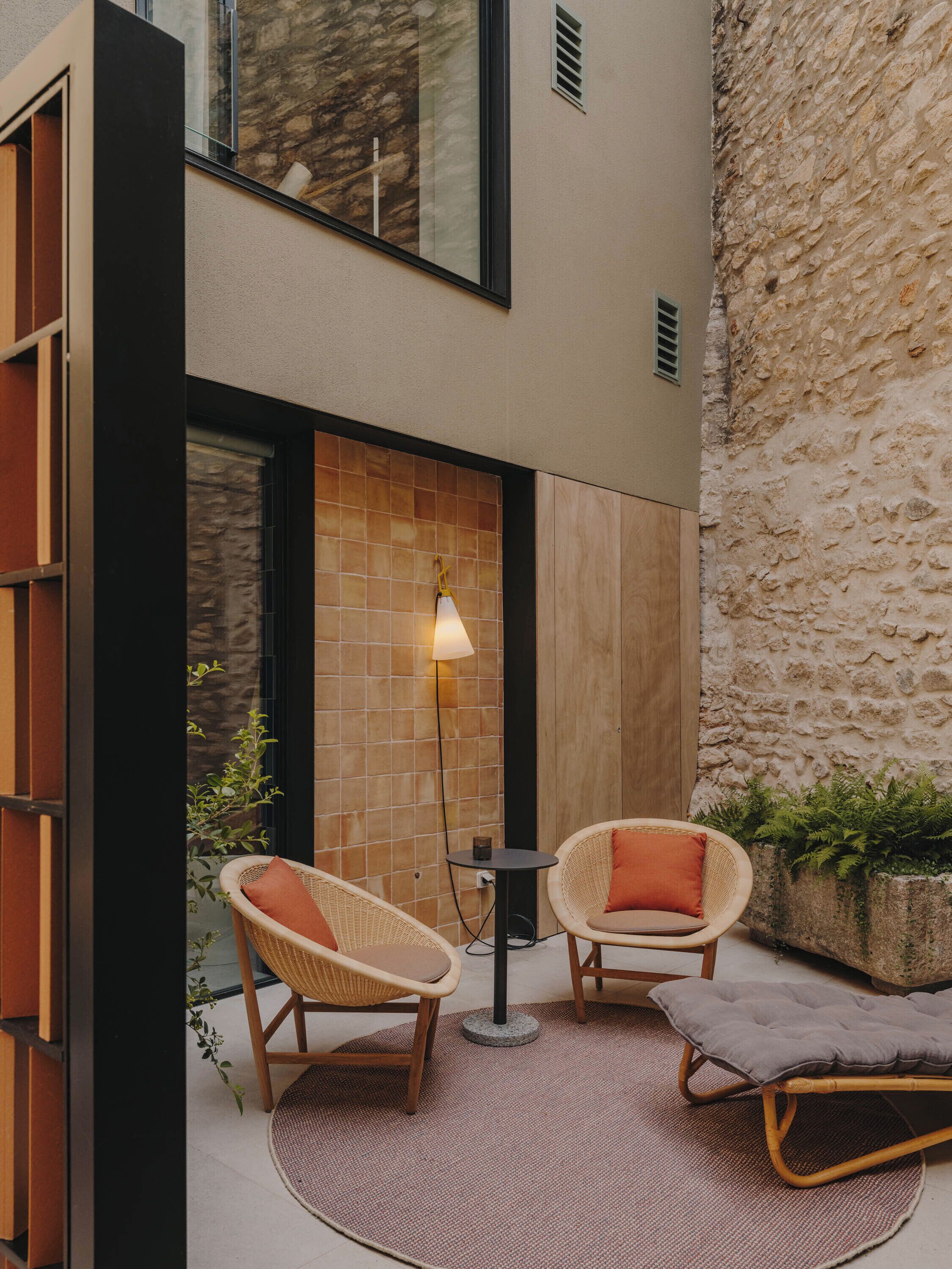 Un espace extérieur accueillant, avec des fauteuils en osier et une petite table, un mur carrelé et un mur de pierres en arrière-plan.