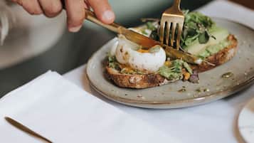 A person using a fork and knife to cut a sandwich on a plate.