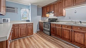 Cocina con gabinetes de madera, microondas, estufa y ventana con persianas.