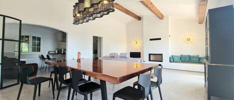 A modern dining area with a wooden table and black chairs, a kitchen in the background, and a living area with a sofa and decorative wall lights.