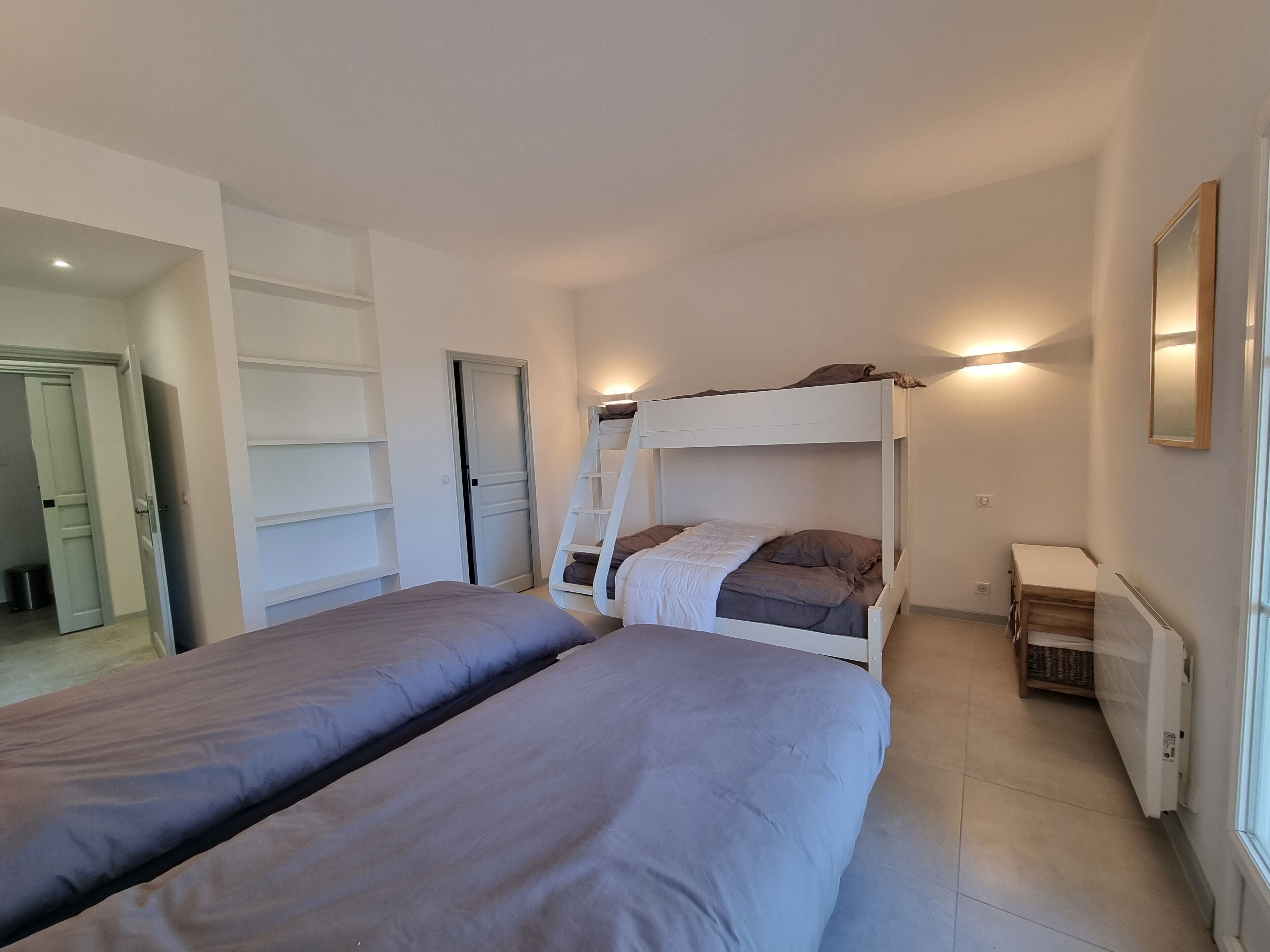 Une chambre avec deux lits, une échelle, un radiateur et une porte donnant sur une autre pièce.