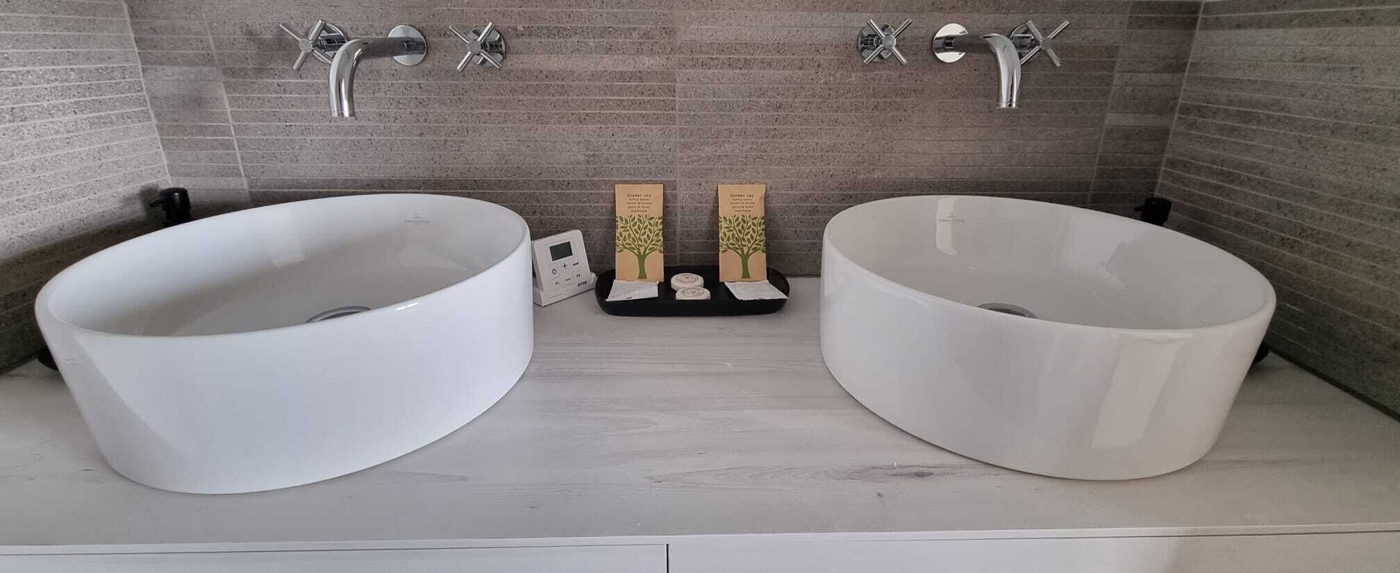 Ein Badezimmer mit zwei großen weißen Waschbecken, einer kleinen digitalen Waage und zwei hölzernen Boxen mit Baummotiven.