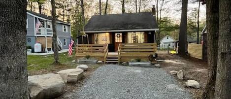 A cabin with a gravel driveway leading to a wooden porch, surrounded by trees.