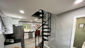 Eine kompakte Küche mit modernen Geräten, ein Essbereich mit einem Holztisch und eine Wendeltreppe, die in eine obere Etage führt.