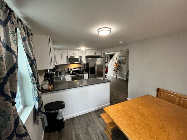 A modern kitchen with white cabinets, stainless steel appliances, and a wooden dining table.
