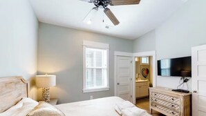 A bedroom with a bed, a ceiling fan, a dresser, a TV, and a window with blinds.