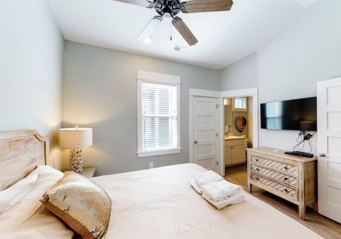 A bedroom with a bed, a ceiling fan, a dresser, a TV, and a window with blinds.