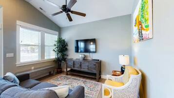 A living room with a ceiling fan, a television, a sofa, a chair, a plant, and a window with blinds.