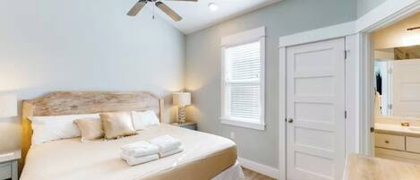 A bedroom with a bed, a ceiling fan, a nightstand, a lamp, a window with blinds, and a door.