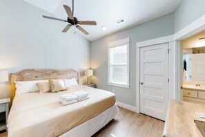 A bedroom with a bed, a ceiling fan, a nightstand, a lamp, a window with blinds, and a door. - The Great Crabsby | Dogs OK! Walk to beach, Pool (Corolla)