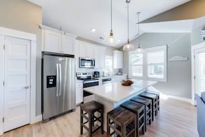 A modern kitchen with white cabinetry, stainless steel appliances, and a central island with stools.