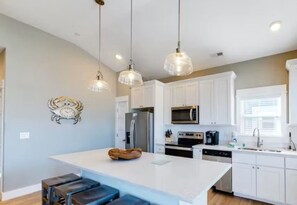 A modern kitchen with white cabinets, a central island, pendant lighting, and a refrigerator.
