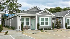 A row of single-story houses with a garage, a covered porch, and a small front yard with a chair and plants. - The Great Crabsby | Dogs OK! Walk to beach, Pool (Corolla)