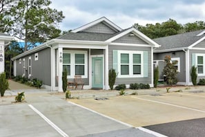 A row of single-story houses with a garage, a covered porch, and a small front yard with a chair and plants. - The Great Crabsby | Dogs OK! Walk to beach, Pool (Corolla)
