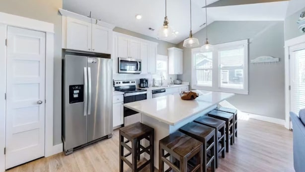 A modern kitchen with white cabinetry, stainless steel appliances, and a central island with stools.