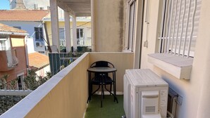 Ein Balkon mit künstlichem Grünrasen, einem kleinen Tisch mit zwei Stühlen und einem weißen Gerät, wahrscheinlich ein Kühlschrank oder Gefriertruhe, an der Wand.