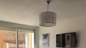 Ein modernes, helles Zimmer mit einem großen Fenster, einem weißen Schrank, einem an der Wand befestigten Fernseher und einem Essbereich mit Tisch und Stühlen.