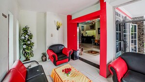 Una sala de estar con muebles rojos y negros, una mesa de centro con flores y vista al comedor.