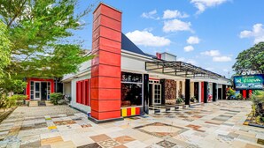 Un edificio con fachada roja y blanca, una amplia entrada de vidrio y un patio empedrado.