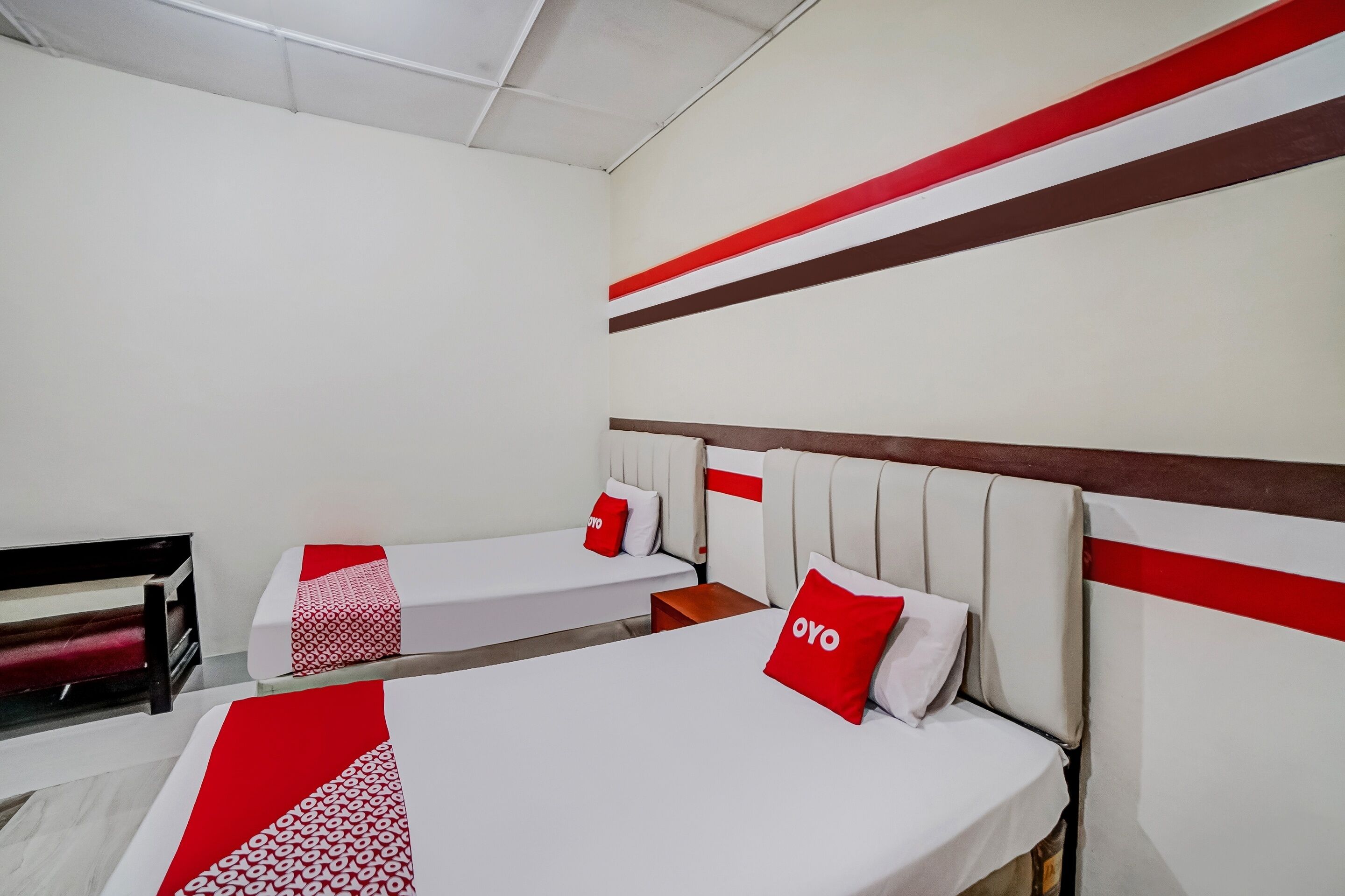 Een hotelkamer met twee bedden, elk met een rode en witte bedspreide en passende kussens. De kamer heeft een modern design met een wit en rood kleurenschema en een houten hoofdbord.