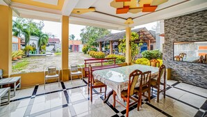 Un comedor con una mesa de vidrio y sillas de madera, un banco, y vista al jardín y edificios exteriores.