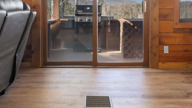 A wooden cabin with a sliding glass door leading to an outdoor deck, a grill, and a chair.