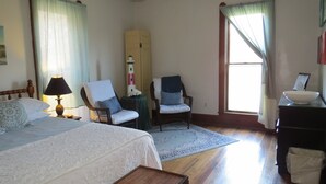 Ein Hotelzimmer mit einem großen Bett, zwei Sesseln, einem Schreibtisch und einem fenster mit Vorhängen.