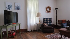 Ein Wohnzimmer mit einem Fernseher auf einem grünen Tisch, einer Lampe, einem blauen Sessel und einem Sofa.