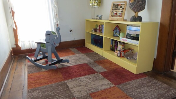 A room with a rocking chair, a bookshelf with various board games, and a patterned rug.