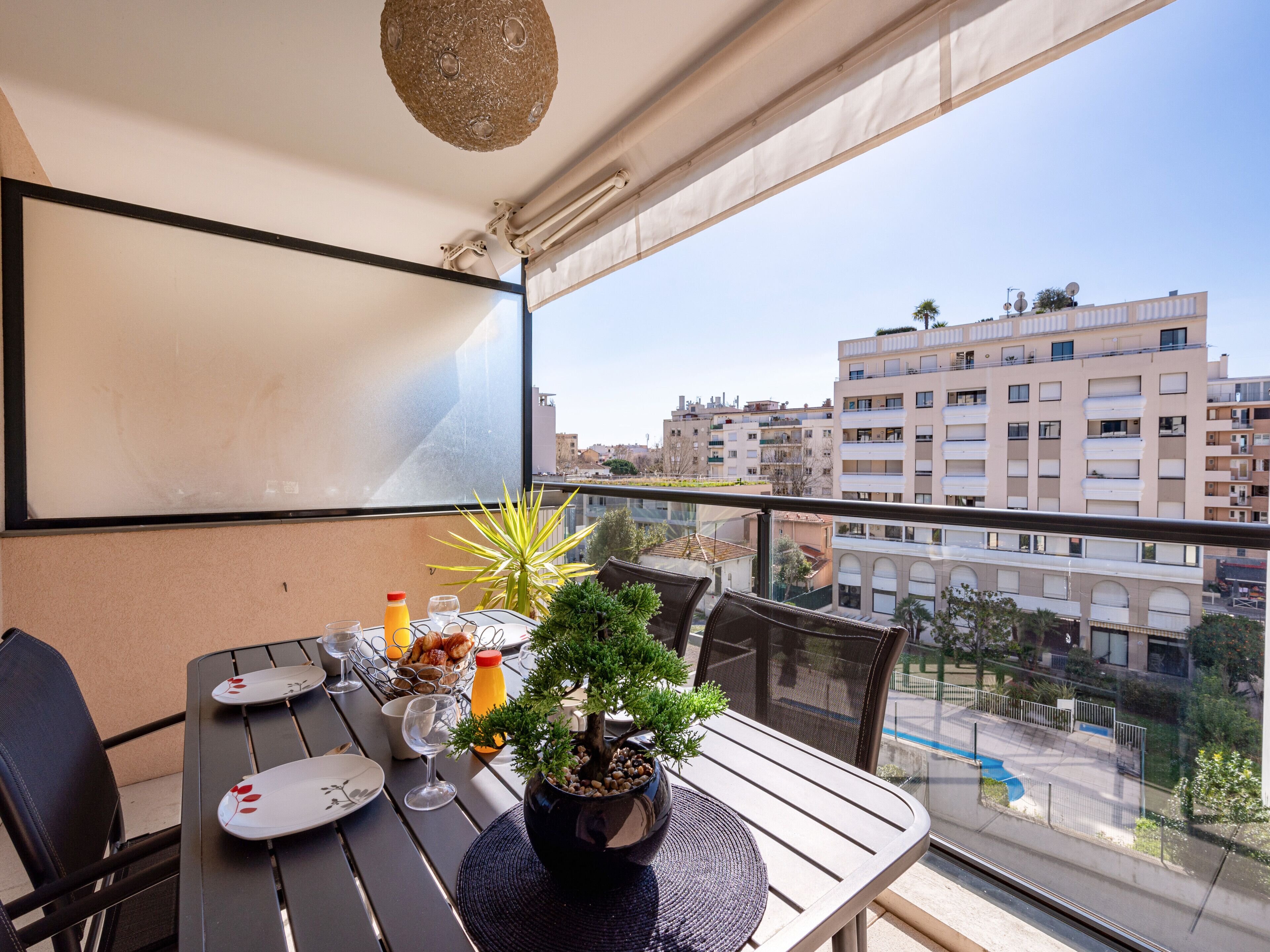Un balcon avec une table dressée pour le dîner, une plante en pot et une vue sur le paysage urbain.