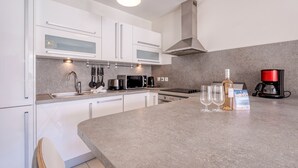 Eine moderne Küche mit weißen Schränken, einer Arbeitsplatte aus Granit, einer Edelstahl-Dunstabzugshaube, einer Kaffeemaschine und Weingläsern.