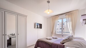 Ein Schlafzimmer mit Bett, Fernseher, Kleiderschrank und einem Fenster mit Vorhängen.