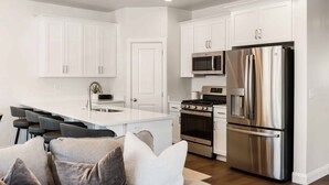 A modern kitchen with white cabinetry, a stainless steel refrigerator, a microwave, and a gas stove. - Life Is Suite 3 Bedroom Home (Washington)