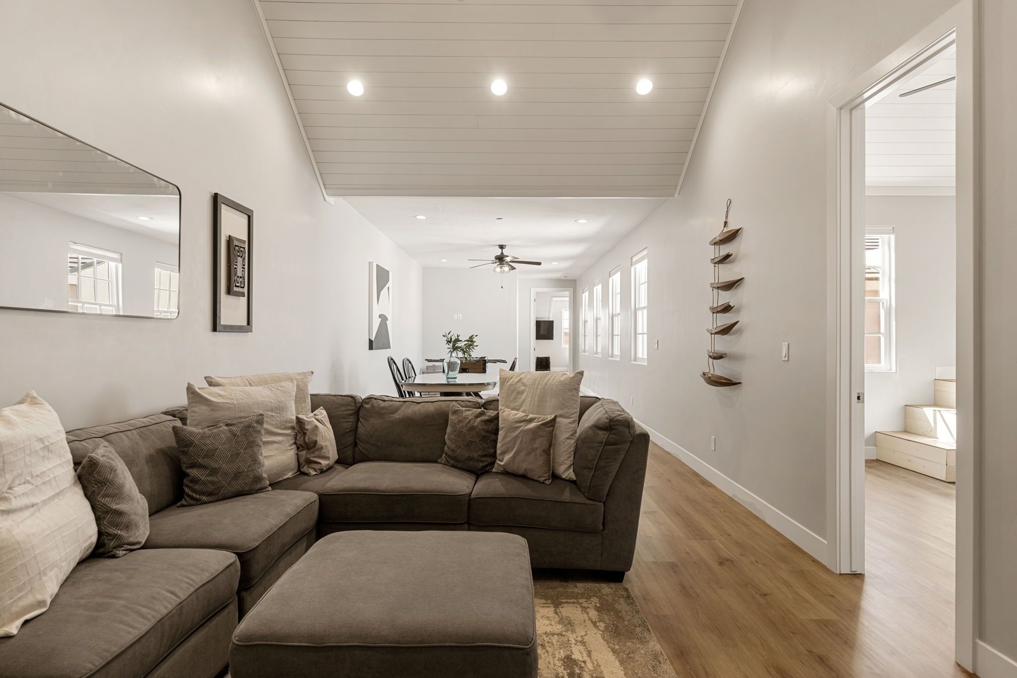 A modern living room with a sectional sofa, a dining area, and a hallway leading to another room.