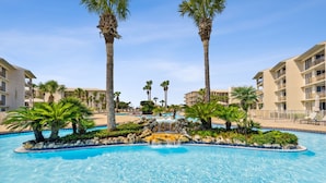A swimming pool with palm trees and a waterfall feature, surrounded by multi-story hotel buildings. - HP 45W What the Heck @ High Pointe | Lagoon Pool | Tennis & Pickleball Courts (High Pointe Resort)